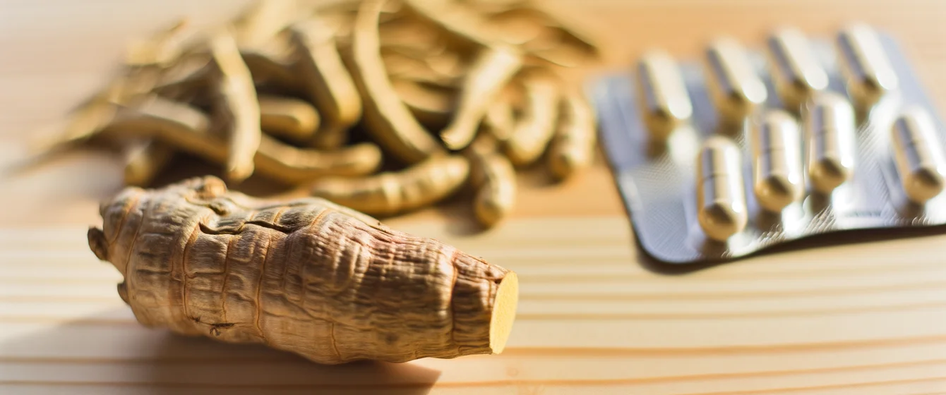 Raíz de ashwagandha junto a cápsulas de suplemento sobre fondo de madera natural